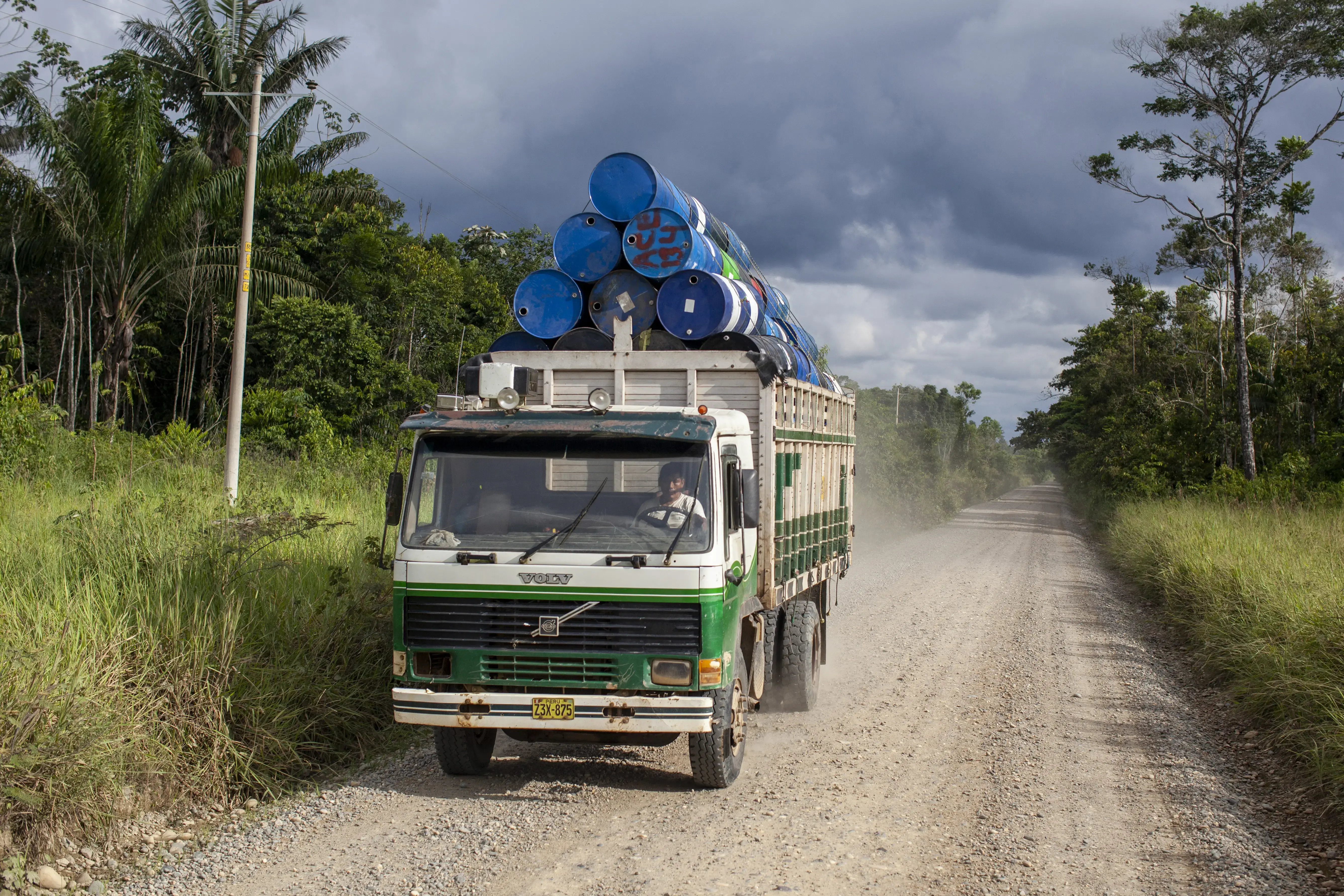 A white-and-green Volvo truck carries a payload of blue-painted barrels, stacked in a pyramid.