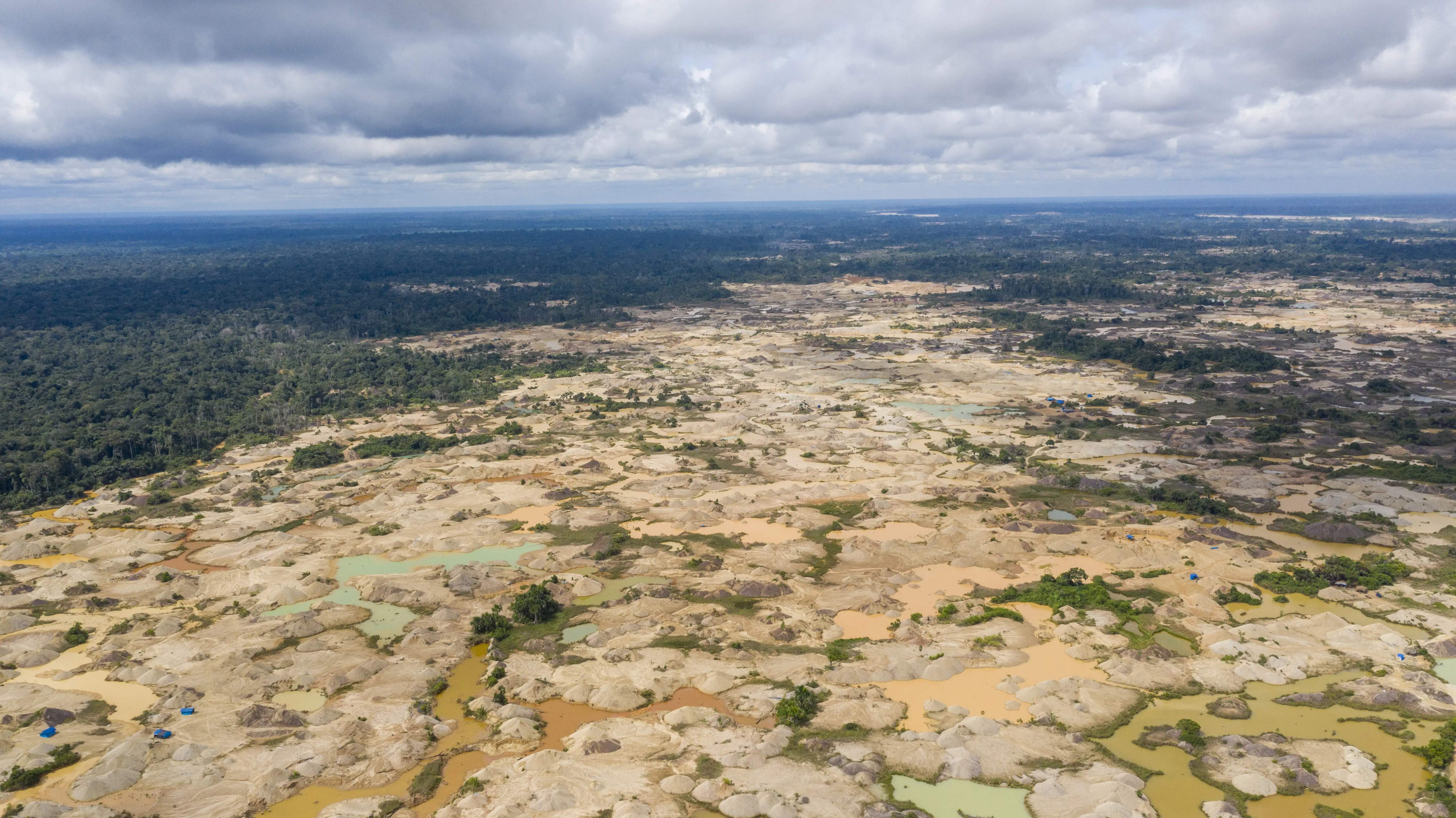A stark, aerial image of mining runoff and deforestation. A mottled beige where there should be lush green.