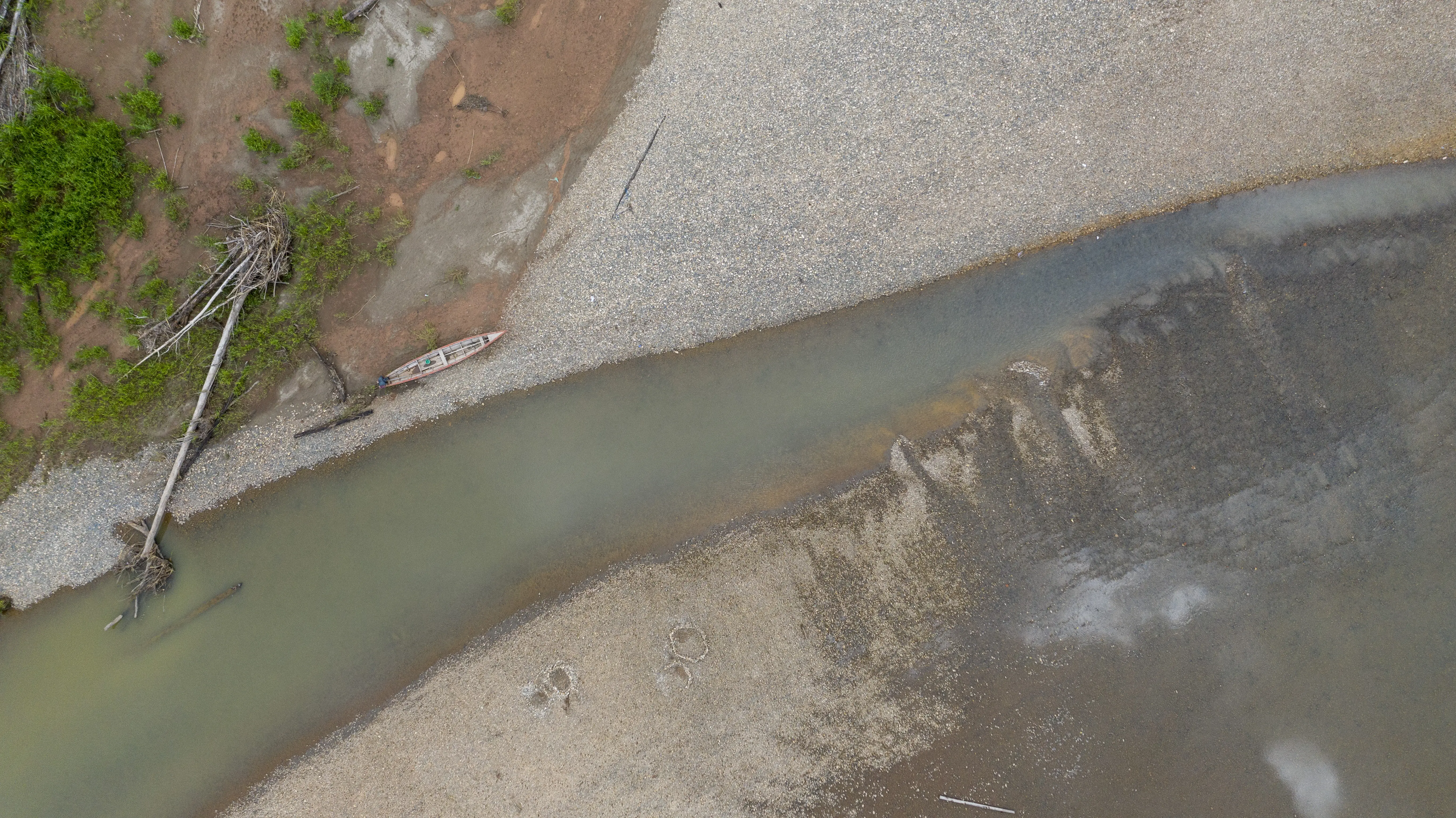 An aerial image of a milky green river, tapering between shores of gravel.