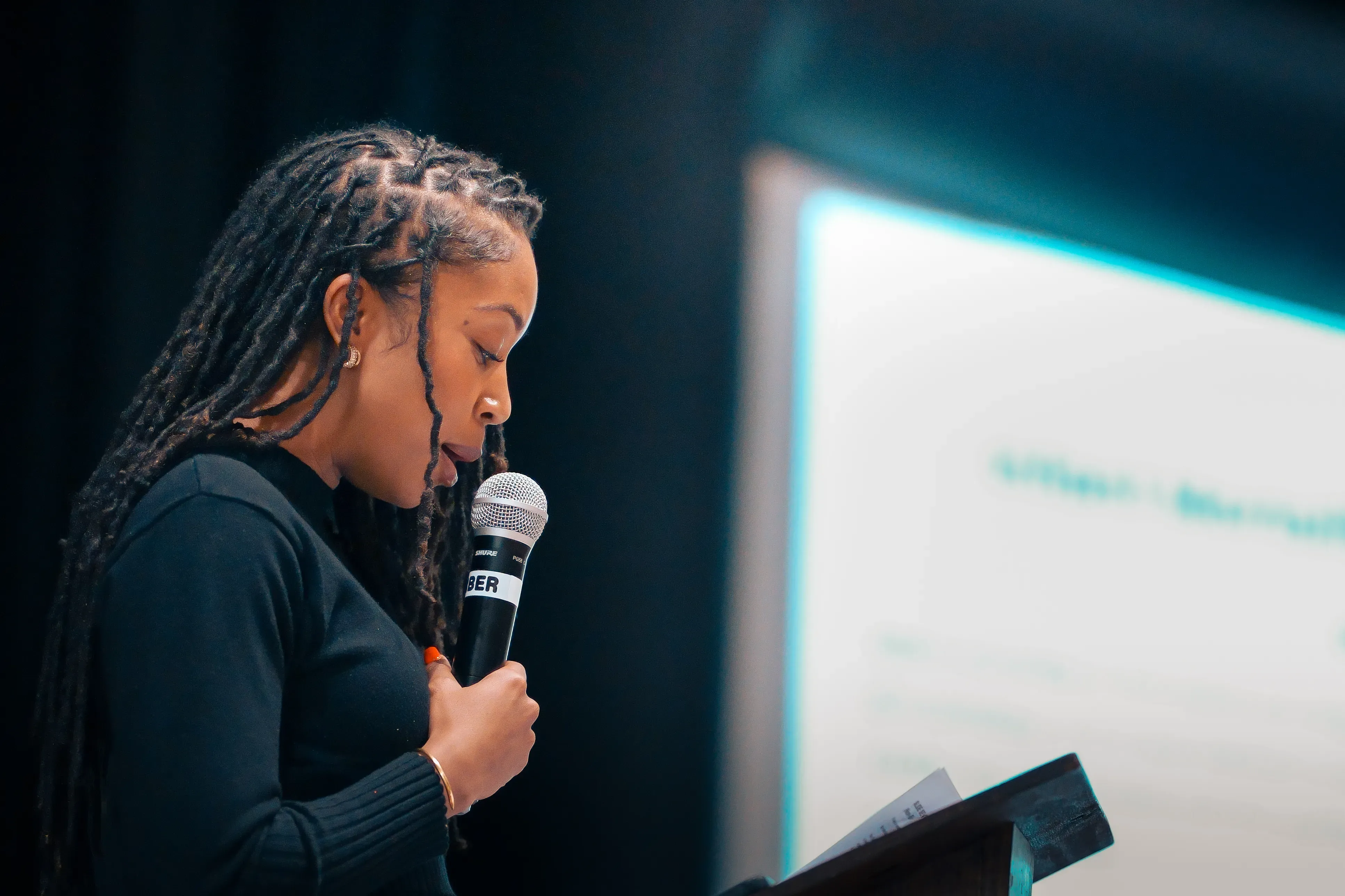 MiaJenell Peake, a Black woman with long locs, holds a microphone during her keynote address.