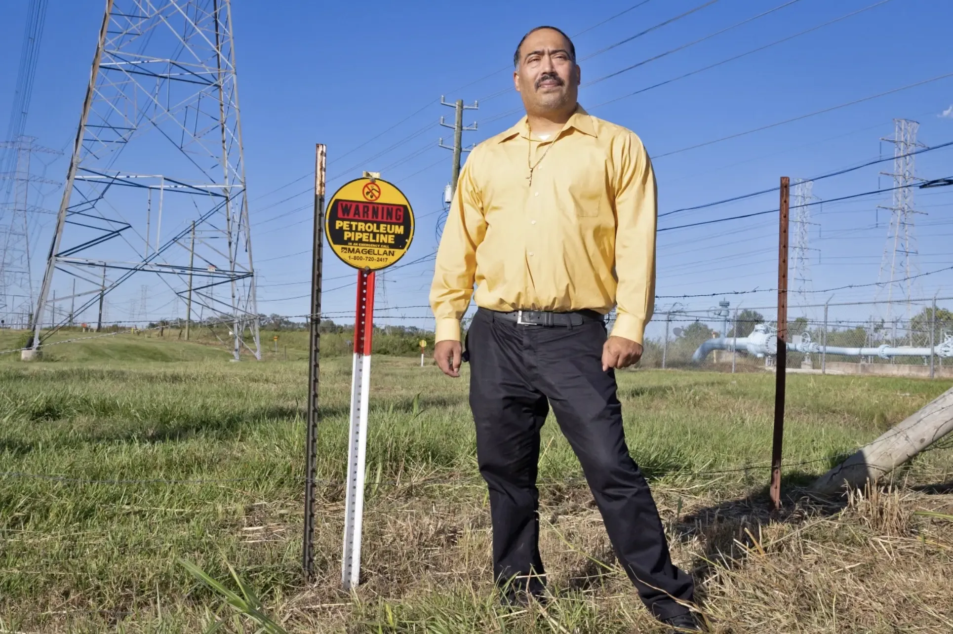 A man stands in front of a pipeline in his hometown next to a warning sign that indicates their pipeline