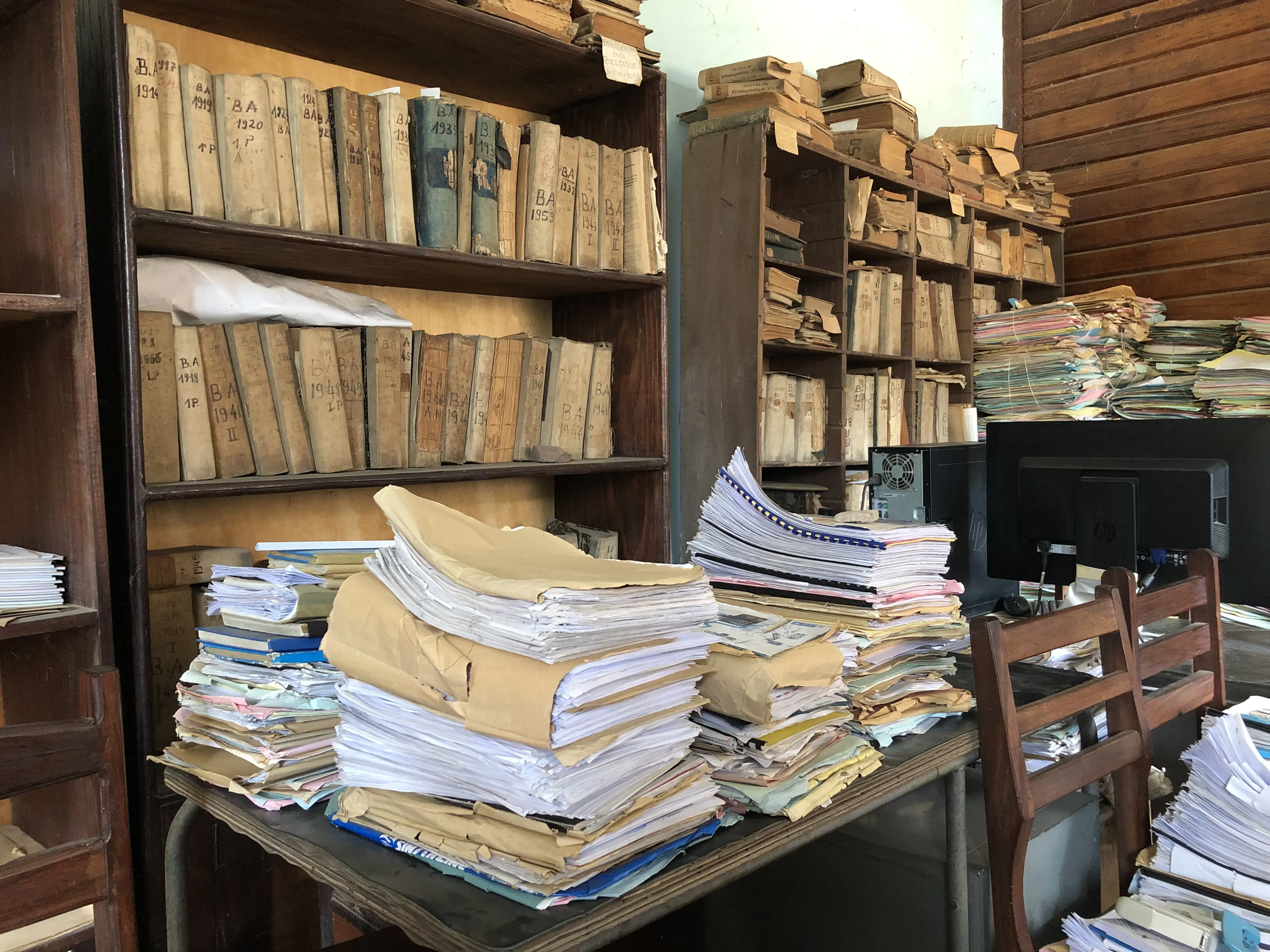 books and papers browned with age sit on shelves and atop a table.