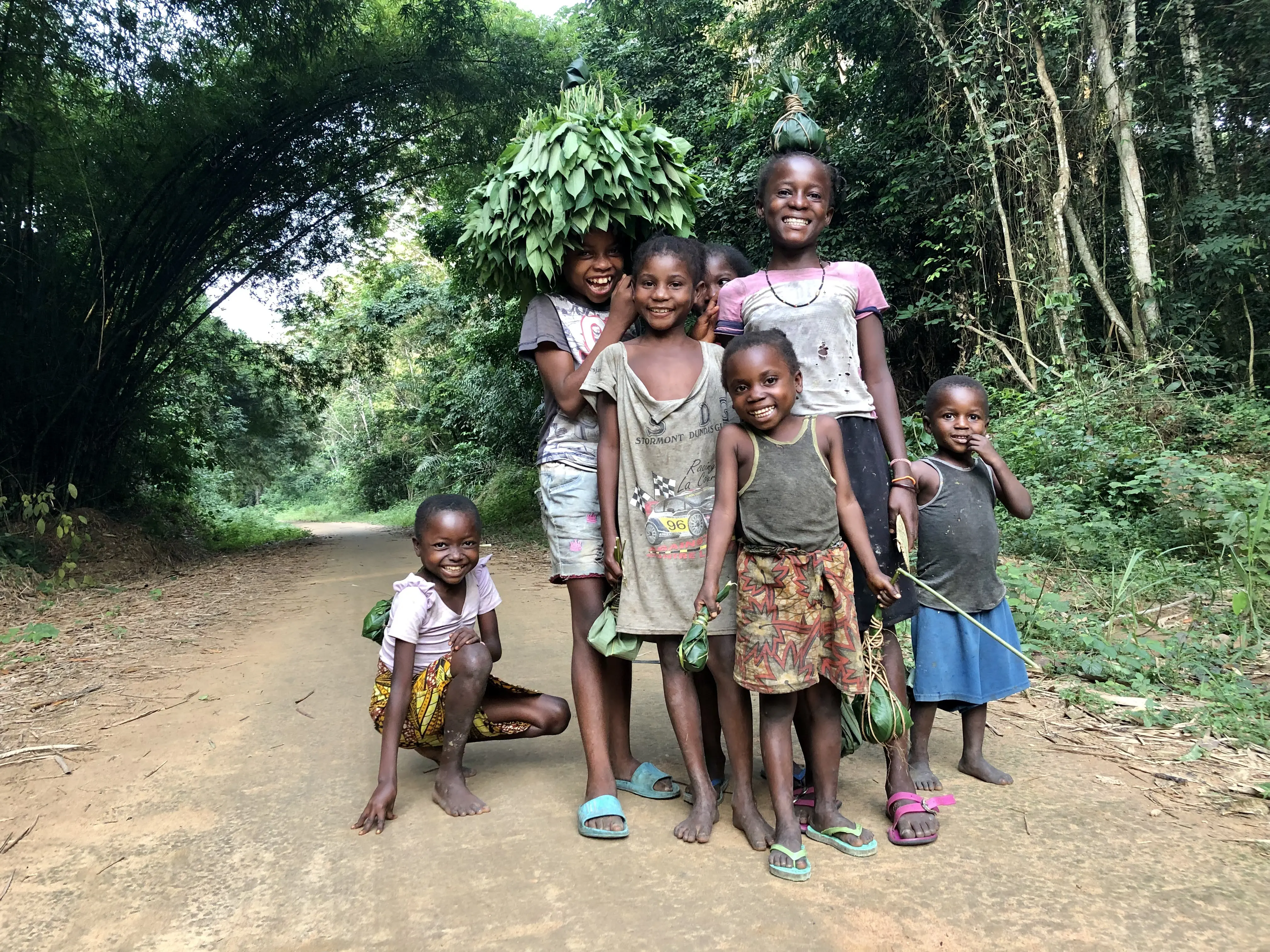 Children pose for a group portrait. one of the children has the bunch of cassava leaves on their head.