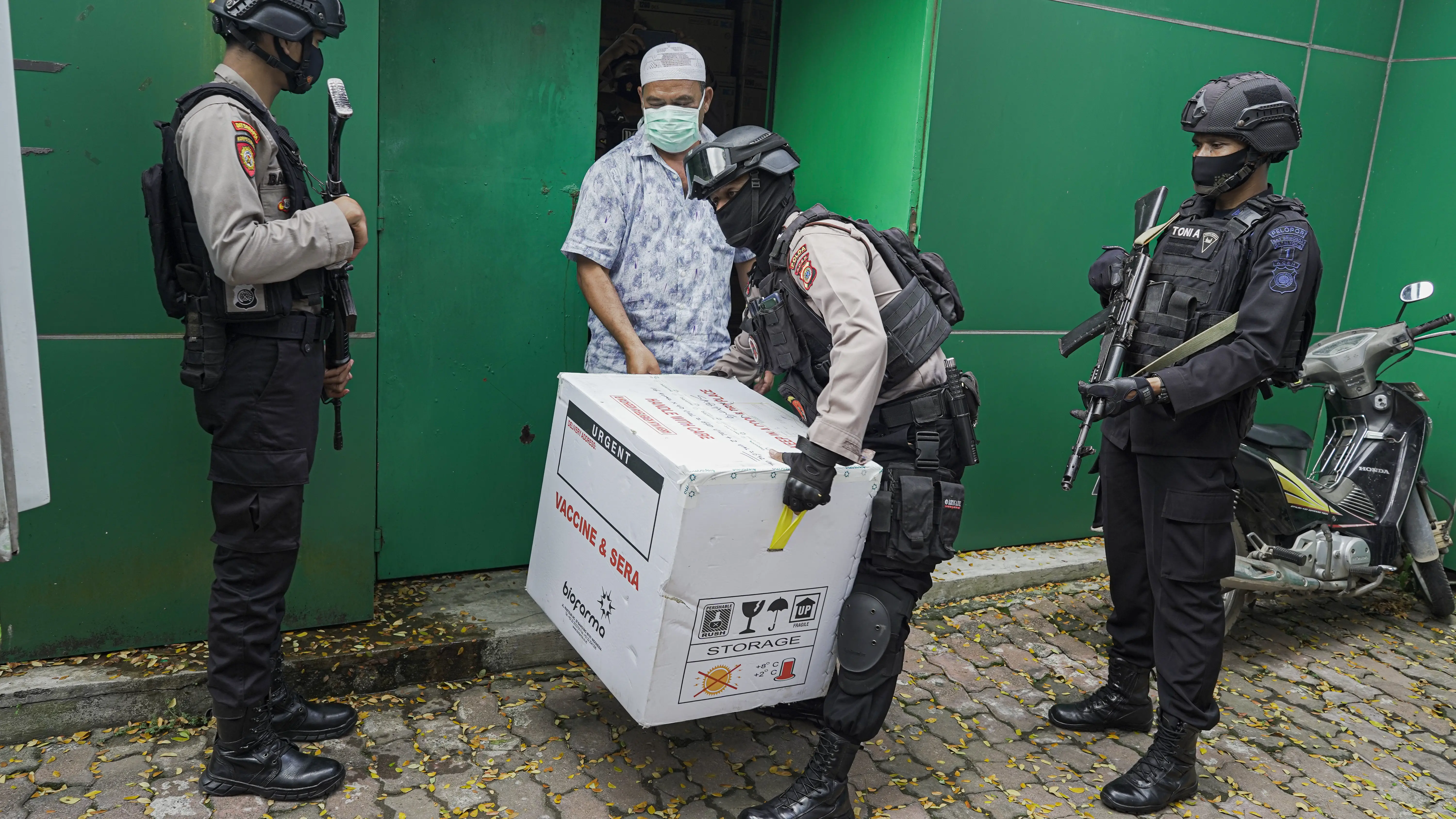 A police officer carries a large box full of vaccines.