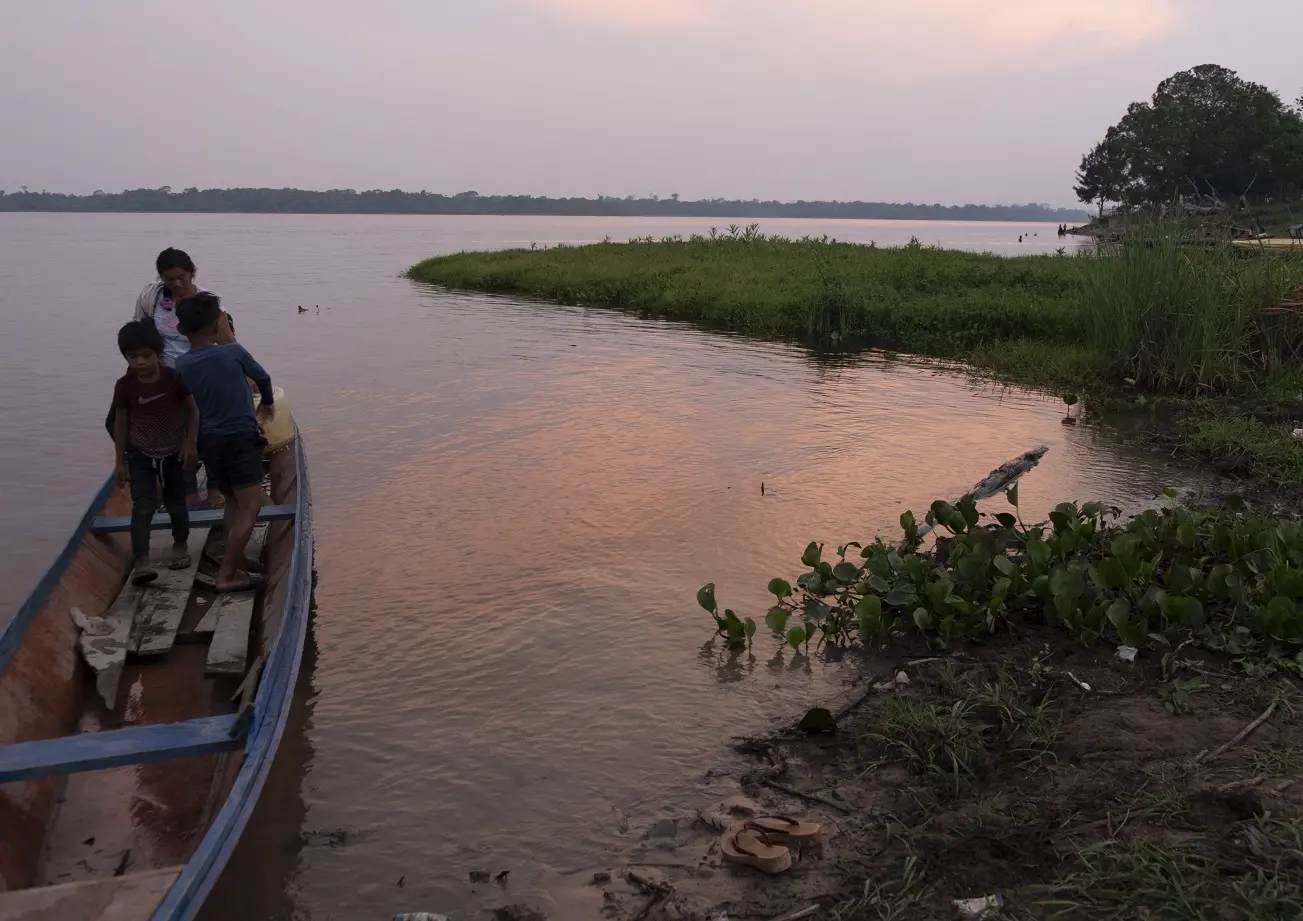 Three people leave a boat as they reach the shoreline. 