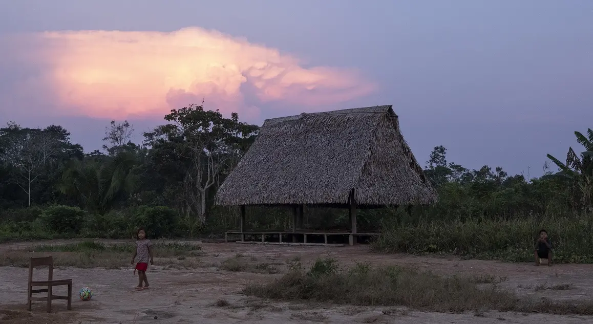 Two children play football as the foreground features a sunset. 