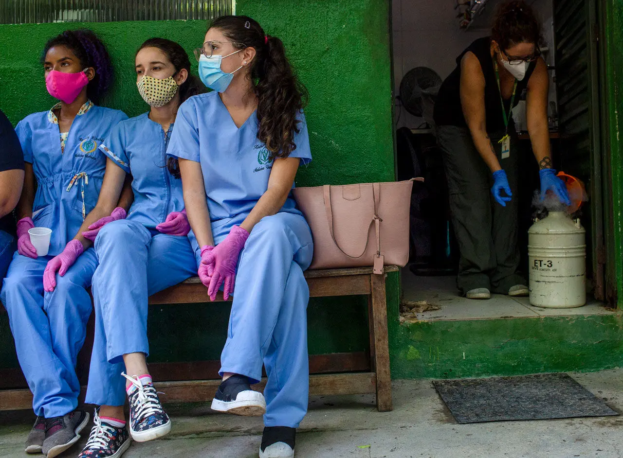 Three people in PPE sit on a bench while a person handles liquid nitrogen behind them in the background.