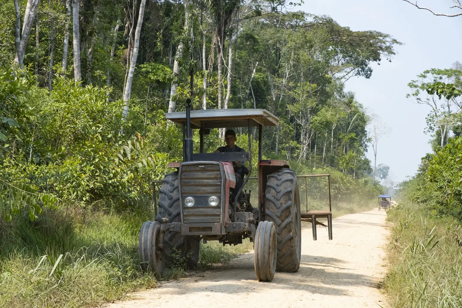 A man drives a tractor on a dusty road. 