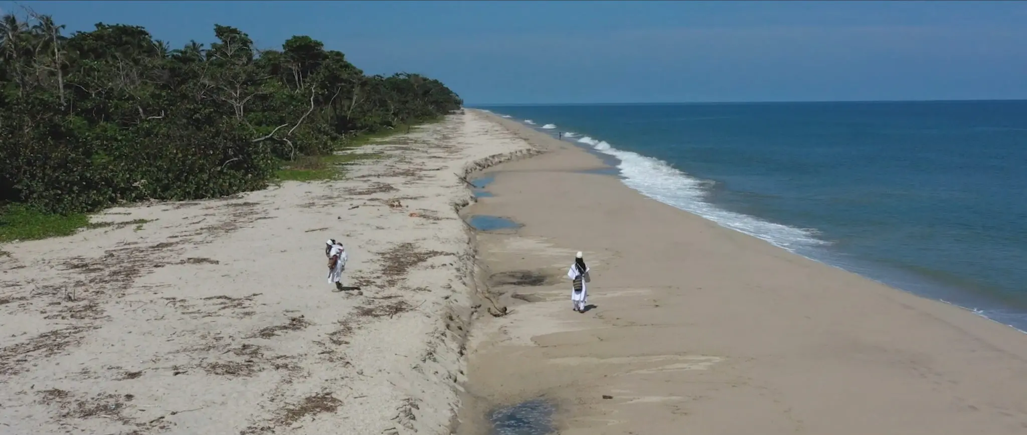 Indigenous people walk alongside the beach