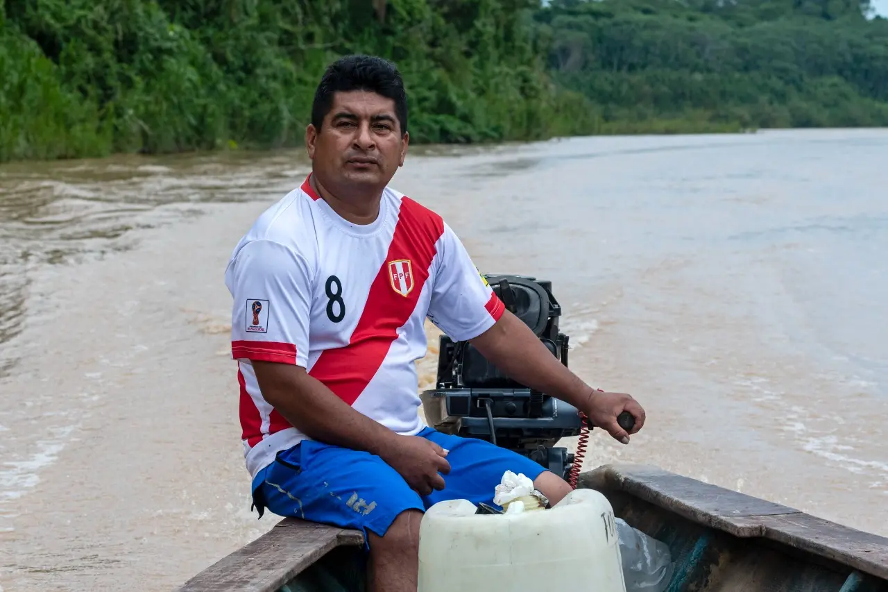 A ma with a Peruvian national football team jersey navigates a river on a motorboat.