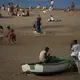 Two migrants sit on a fishing boat as people enjoy the beach in Gran Canaria island, Spain, on Friday, Aug. 21, 2020.&nbsp;Image by Emilio Morenatti/AP Photo. Spain, 2020.