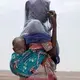 In this July 23, 2019 photo, Fatma, a migrant from Mali, carries her one-year-old Said Yaacoub, as she makes her way in Lahj, Yemen. Fatma and her family of four are slow because of the children. They came by boat from Djibouti and dream of going Saudi Arabia. They were taken to the lockups known in Arabic as 'hosh' but smugglers let them go because of the children. Image by Nariman El-Mofty / AP Photo. Yemen, 2019.