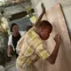 Baron Ritcharmant, 9, right, and his brother Celestin Shneider, 7, with the encouragement of their mother Edrice Elvige, write out their math homework in chalk in the backyard of the family's home in the Canaan 4 neighborhood. An active community organizer since she moved to Canaan in 2010, Elvige dreams of a center where the neighborhood children can go for activities and basic health care. Image by Allison Shelley. Haiti, 2019.